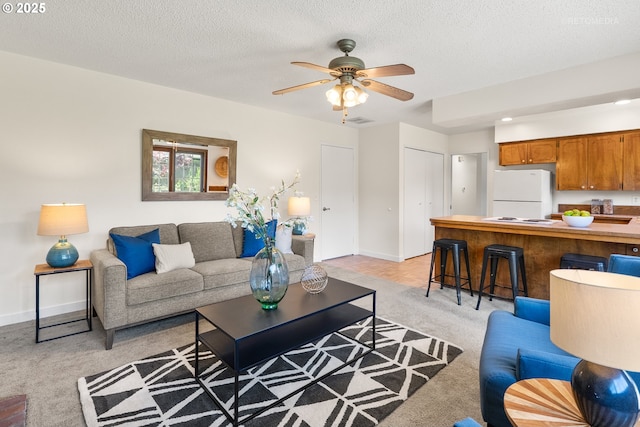 living room featuring light colored carpet, ceiling fan, a textured ceiling, and baseboards