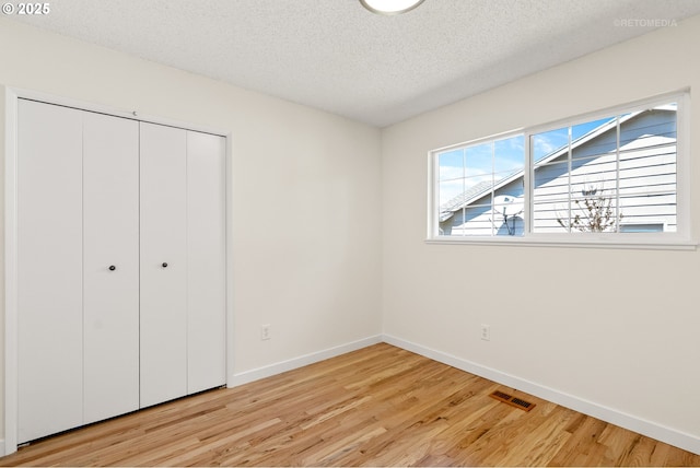 unfurnished bedroom featuring light wood-style floors, baseboards, a textured ceiling, and a closet