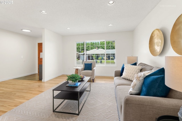 living room featuring light wood-style floors, recessed lighting, a textured ceiling, and baseboards