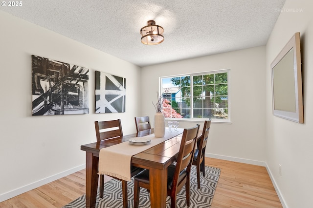 dining area featuring a textured ceiling, light wood-style flooring, and baseboards