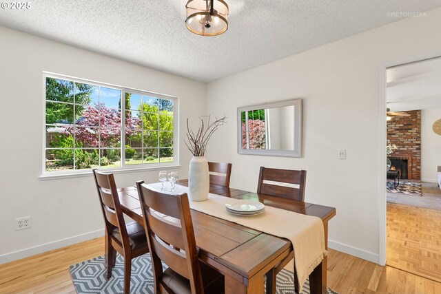 dining space with baseboards, a textured ceiling, light wood-style flooring, and a brick fireplace