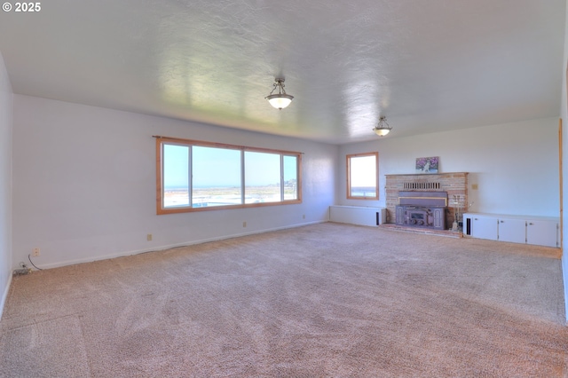 unfurnished living room with carpet flooring, baseboards, and a fireplace with raised hearth