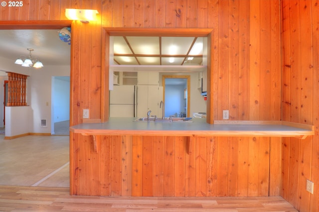 kitchen featuring freestanding refrigerator, a sink, wooden walls, wood finished floors, and a chandelier