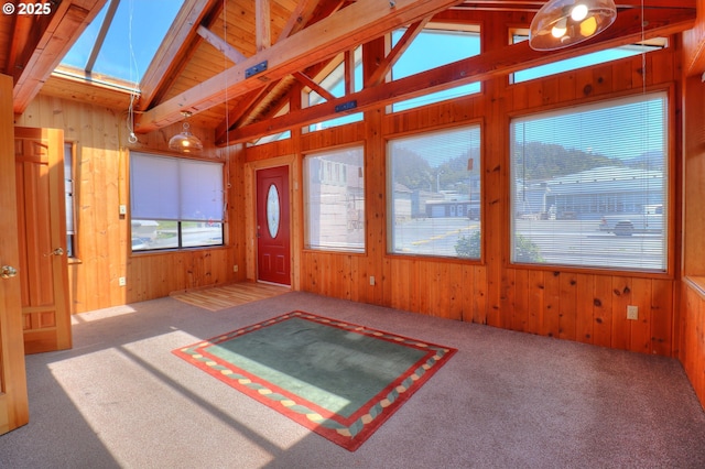 unfurnished living room with wood walls, a skylight, healthy amount of natural light, and carpet