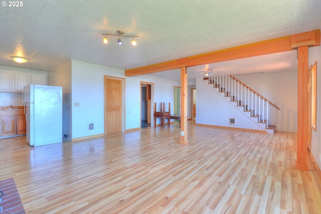 unfurnished living room with light wood-style flooring, stairway, and baseboards