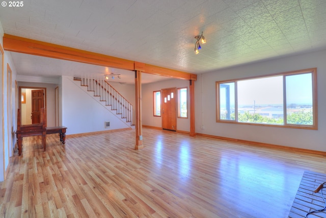 unfurnished living room with stairs, light wood-type flooring, and baseboards