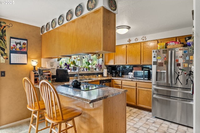 kitchen featuring appliances with stainless steel finishes, a peninsula, brown cabinets, a sink, and a breakfast bar