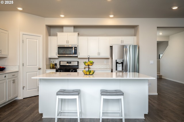 kitchen with a kitchen island, dark wood-type flooring, a breakfast bar area, light countertops, and appliances with stainless steel finishes