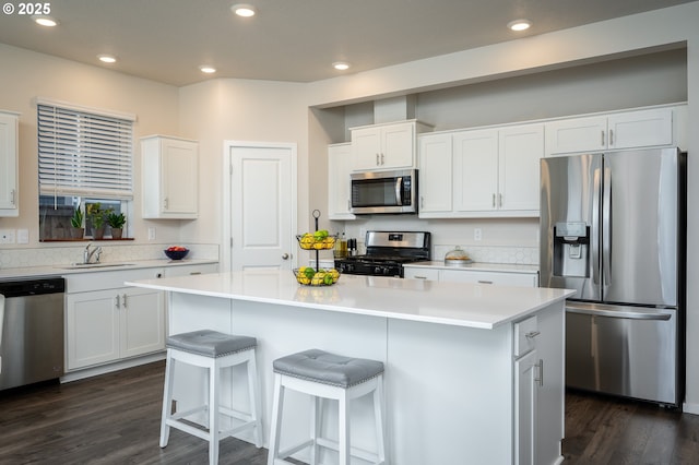 kitchen featuring a kitchen island, a breakfast bar, a sink, white cabinets, and appliances with stainless steel finishes