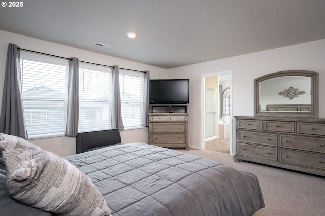 bedroom with connected bathroom, light colored carpet, and a textured ceiling