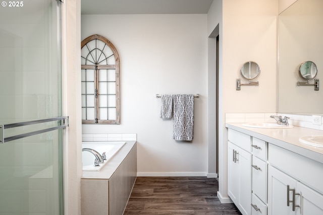 full bath featuring baseboards, double vanity, wood finished floors, a bath, and a sink