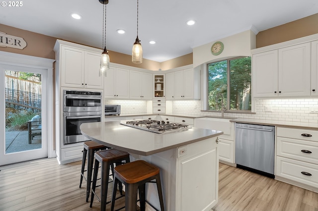 11712 Finnegans Way, Oregon City, OR 97045 - kitchen with appliances with stainless steel finishes, a kitchen breakfast bar, white cabinetry, tasteful backsplash, and light wood-type flooring