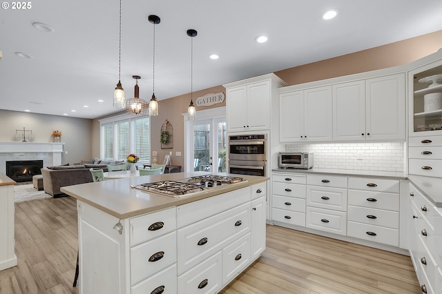 11712 Finnegans Way, Oregon City, OR 97045 - kitchen featuring appliances with stainless steel finishes, a center island, light wood-style flooring, backsplash, and white cabinets
