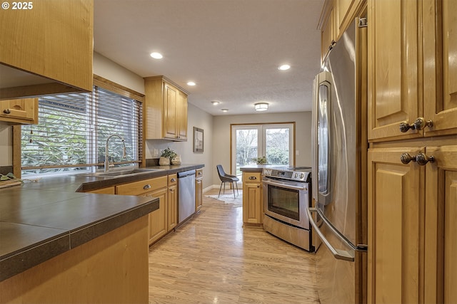 kitchen featuring a sink, light wood-type flooring, dark countertops, recessed lighting, and stainless steel appliances