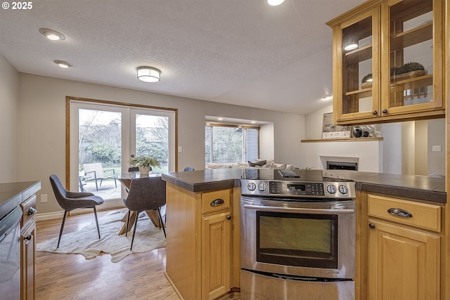 kitchen featuring glass insert cabinets, appliances with stainless steel finishes, a peninsula, light wood-style floors, and a fireplace