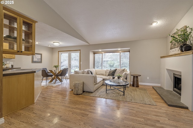 living area featuring a fireplace with raised hearth, light wood-style flooring, a textured ceiling, and lofted ceiling