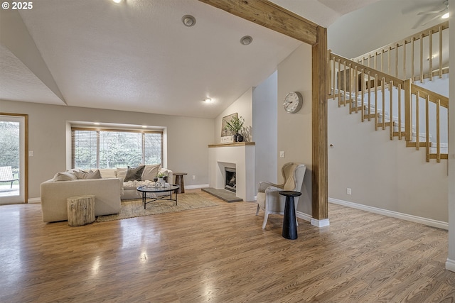 living area featuring wood finished floors, beamed ceiling, baseboards, and stairs