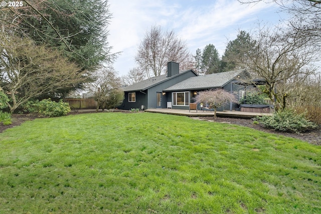 back of house with a hot tub, fence, a chimney, a deck, and a yard