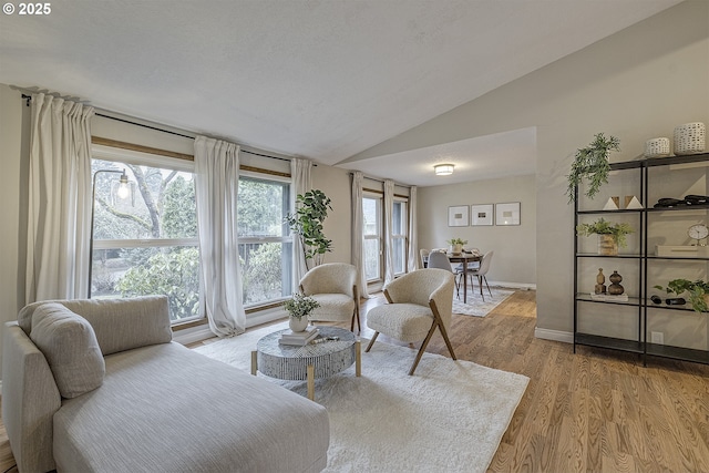 living area featuring baseboards, light wood-type flooring, and vaulted ceiling