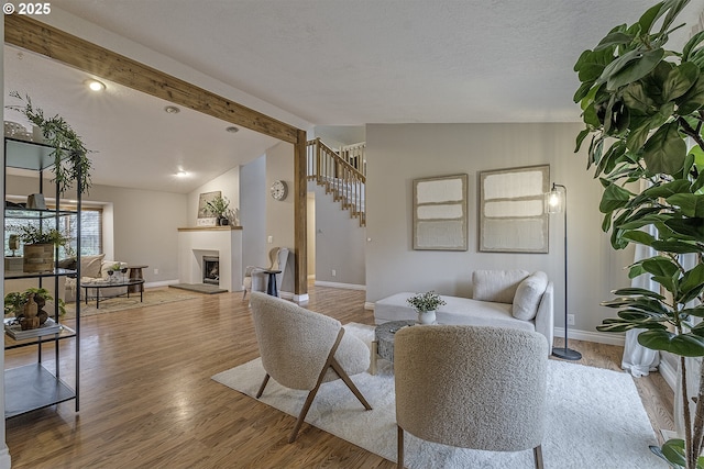 living room with a fireplace with raised hearth, vaulted ceiling with beams, baseboards, stairway, and wood finished floors