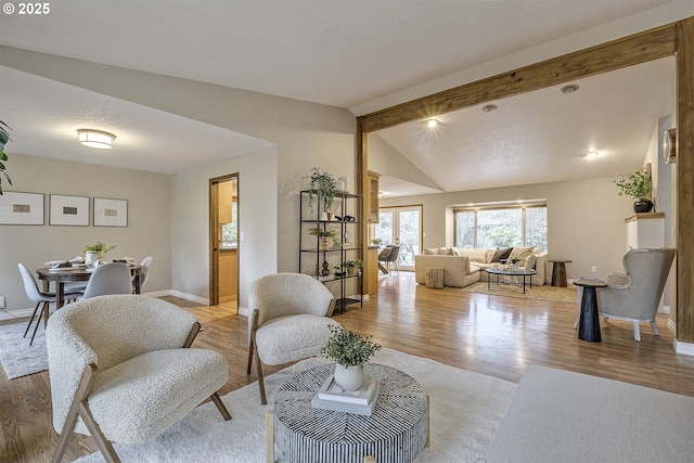 living area featuring lofted ceiling with beams, light wood-type flooring, and baseboards