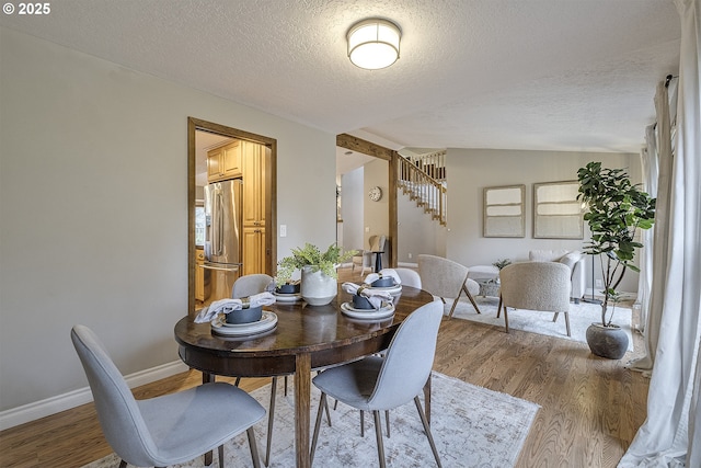 dining area featuring a textured ceiling, wood finished floors, baseboards, and lofted ceiling