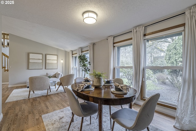 dining area featuring light wood-style flooring, a textured ceiling, baseboards, and lofted ceiling