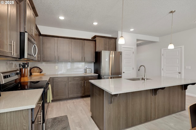 kitchen with sink, hanging light fixtures, stainless steel appliances, backsplash, and a kitchen island with sink