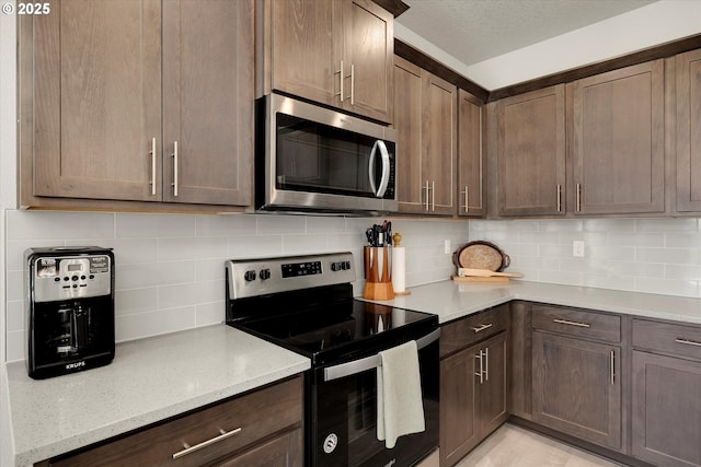 kitchen with decorative backsplash, light stone counters, dark brown cabinets, and stainless steel appliances