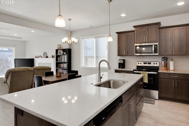 kitchen with light stone countertops, sink, backsplash, a kitchen island with sink, and appliances with stainless steel finishes