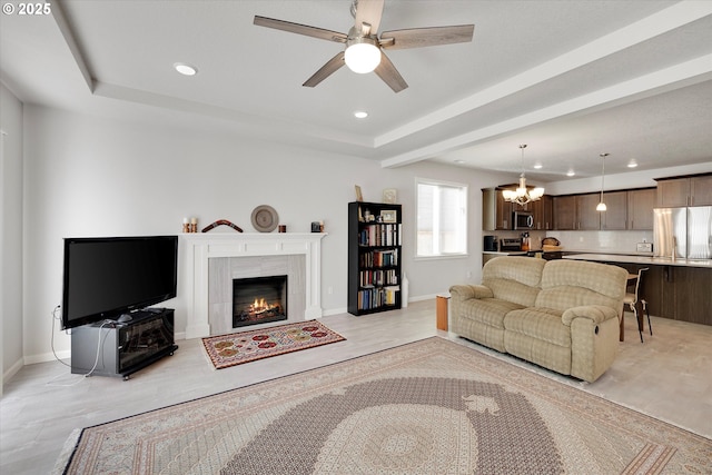 living room featuring ceiling fan with notable chandelier, a high end fireplace, and a tray ceiling