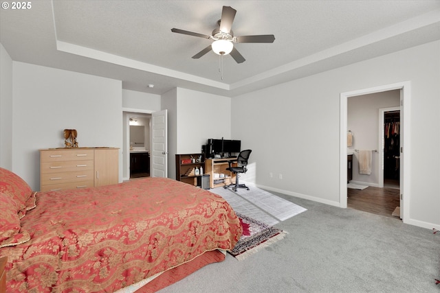 bedroom with a tray ceiling, carpet floors, ensuite bathroom, and ceiling fan