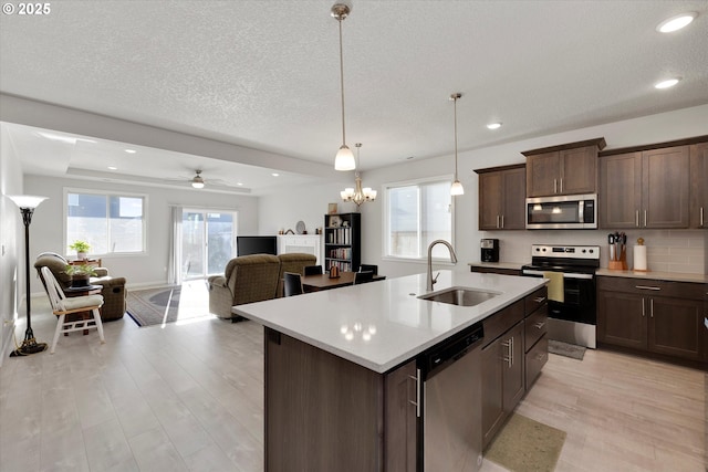 kitchen featuring appliances with stainless steel finishes, dark brown cabinetry, a kitchen island with sink, sink, and pendant lighting