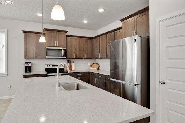 kitchen with pendant lighting, stainless steel appliances, light stone counters, and sink