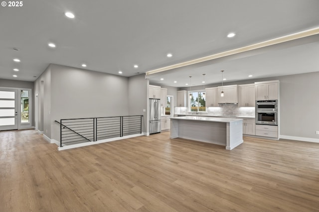 kitchen with hanging light fixtures, appliances with stainless steel finishes, a kitchen island, decorative backsplash, and white cabinets