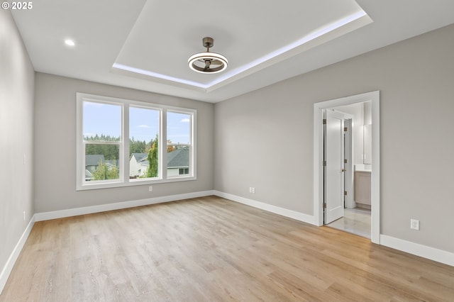 empty room with light hardwood / wood-style floors and a tray ceiling