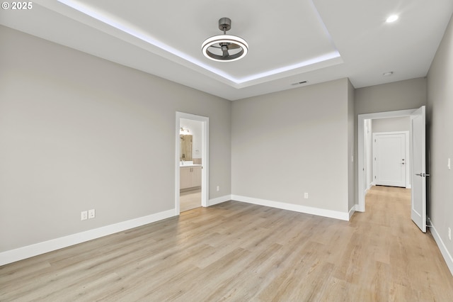 unfurnished bedroom featuring connected bathroom, a raised ceiling, and light wood-type flooring