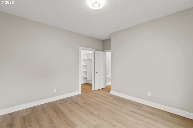 unfurnished bedroom with a spacious closet, a textured ceiling, light wood-type flooring, and a closet