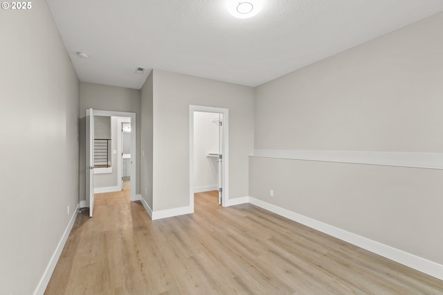 unfurnished bedroom with a closet, a walk in closet, a textured ceiling, and light hardwood / wood-style flooring