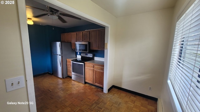 kitchen featuring ceiling fan, brown cabinetry, baseboards, and stainless steel appliances