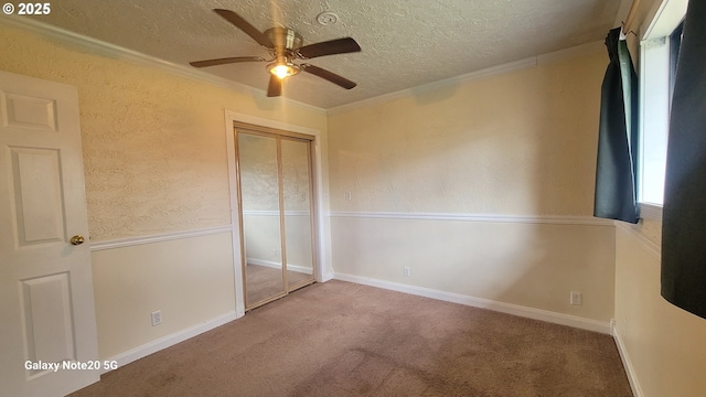 unfurnished bedroom featuring a textured ceiling, a closet, carpet floors, crown molding, and ceiling fan