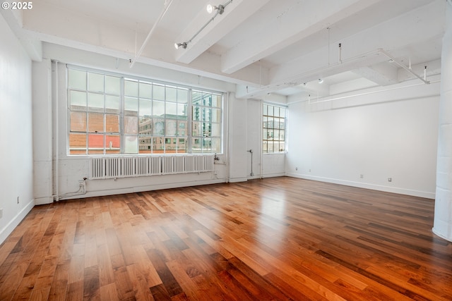 spare room with baseboards, beam ceiling, wood finished floors, and radiator heating unit