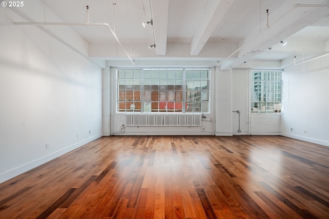 spare room featuring beam ceiling, radiator, wood finished floors, and baseboards