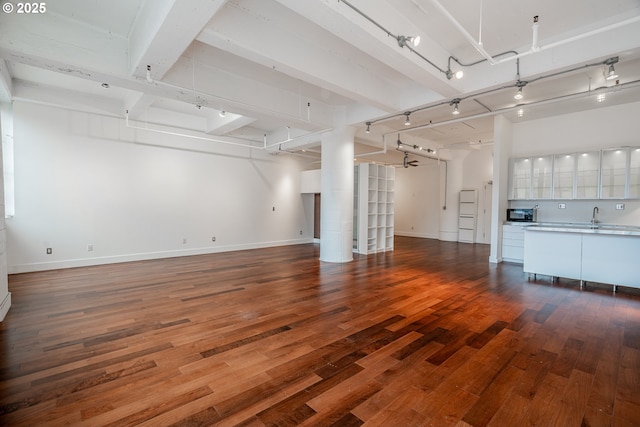 unfurnished living room with track lighting, baseboards, beamed ceiling, wood-type flooring, and a sink