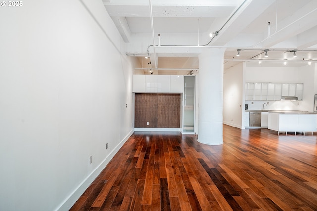 unfurnished living room with dark wood finished floors, rail lighting, and baseboards