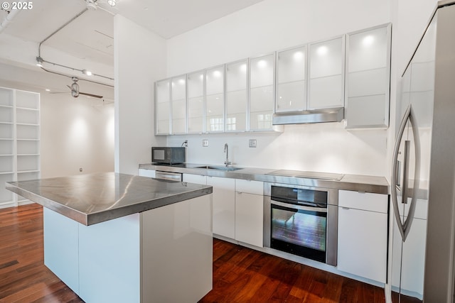 kitchen with stainless steel countertops, under cabinet range hood, appliances with stainless steel finishes, white cabinetry, and a sink