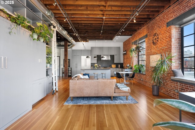 living room featuring a towering ceiling, light wood-type flooring, track lighting, and brick wall