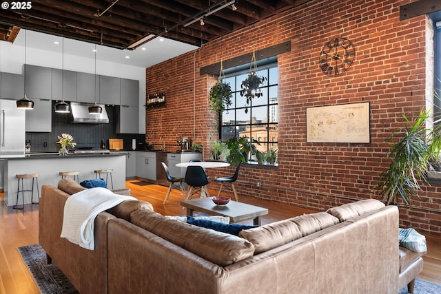 living room with rail lighting, brick wall, a towering ceiling, and light wood-type flooring