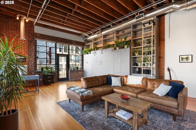 living room with wood-type flooring, brick wall, and a towering ceiling