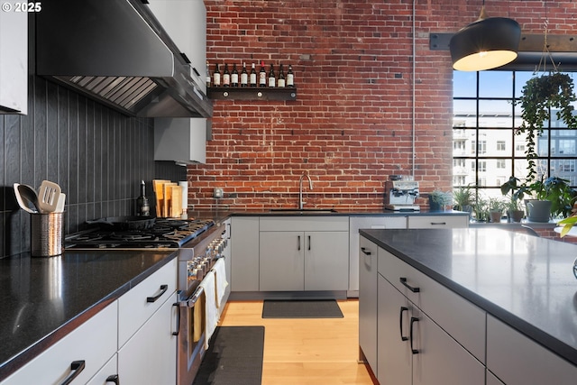 kitchen featuring sink, tasteful backsplash, light hardwood / wood-style flooring, brick wall, and white cabinets